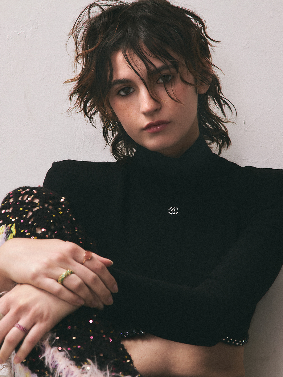 Model leaning aginst a white wall with natural makeup looking at the camera in a relaxed disposition